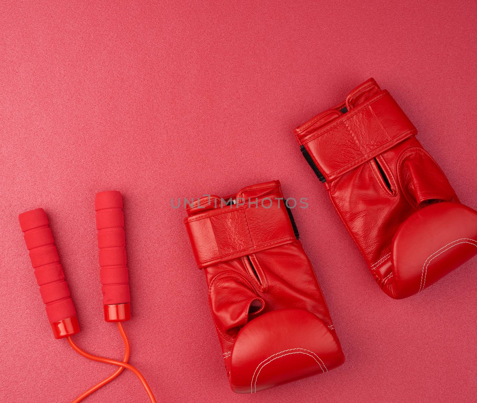 pair of red leather boxing gloves and red jump rope on a neoprene mat, sports set, top view