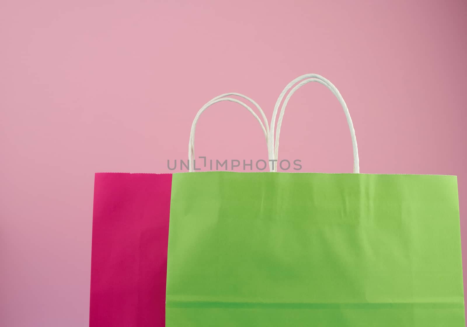 empty multicolored paper bags for shopping and gifts with white handles stand on a pink background