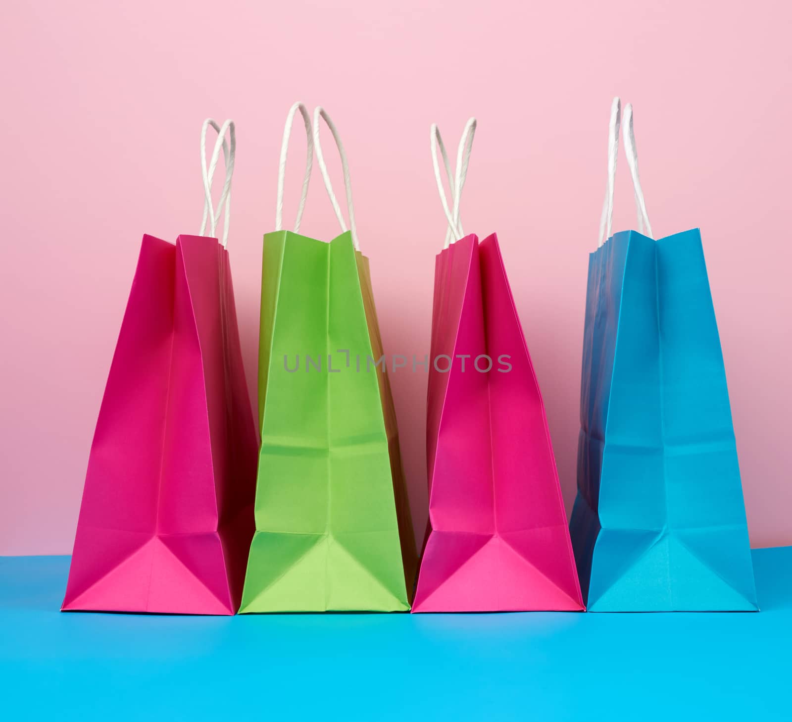 multicolored paper bags for shopping and gifts with white handles stand on a pink-blue background