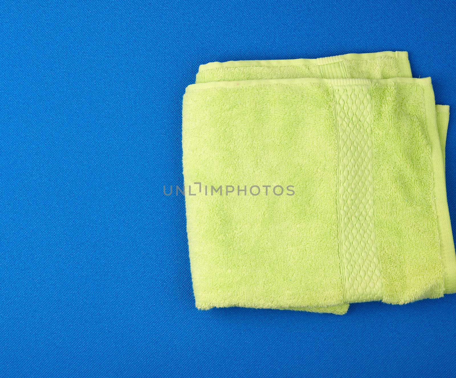 folded bath terry light green towel on a blue background, top view