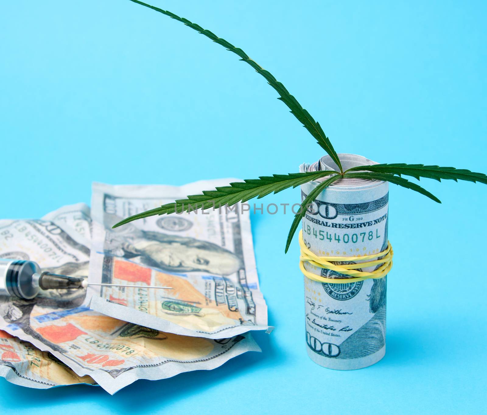 folded cash US dollars, green hemp leaf and empty plastic syringe, drug addiction concept