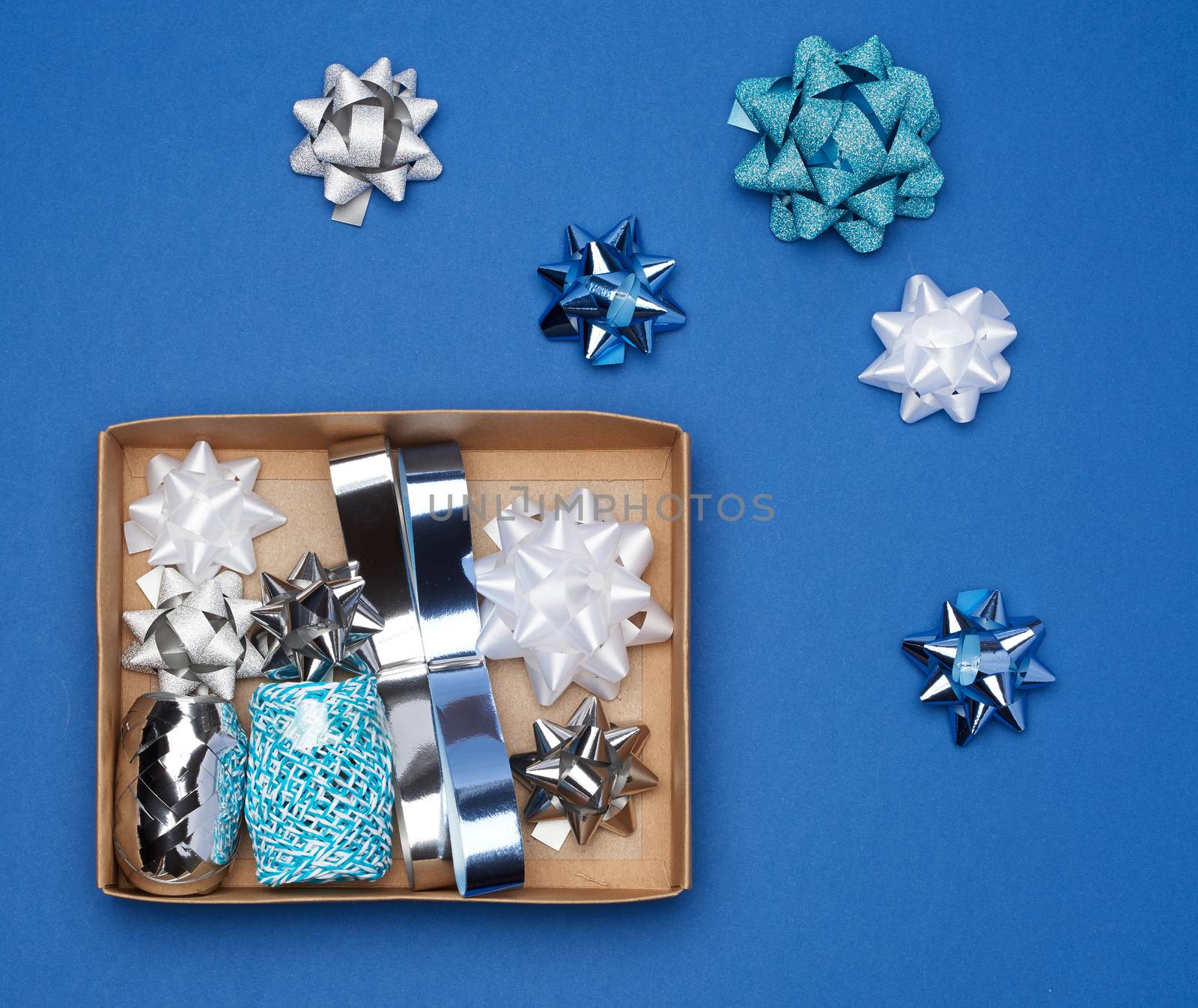 brown cardboard box with a set of decor ribbons and bows for wrapping gifts on a dark blue background, top view