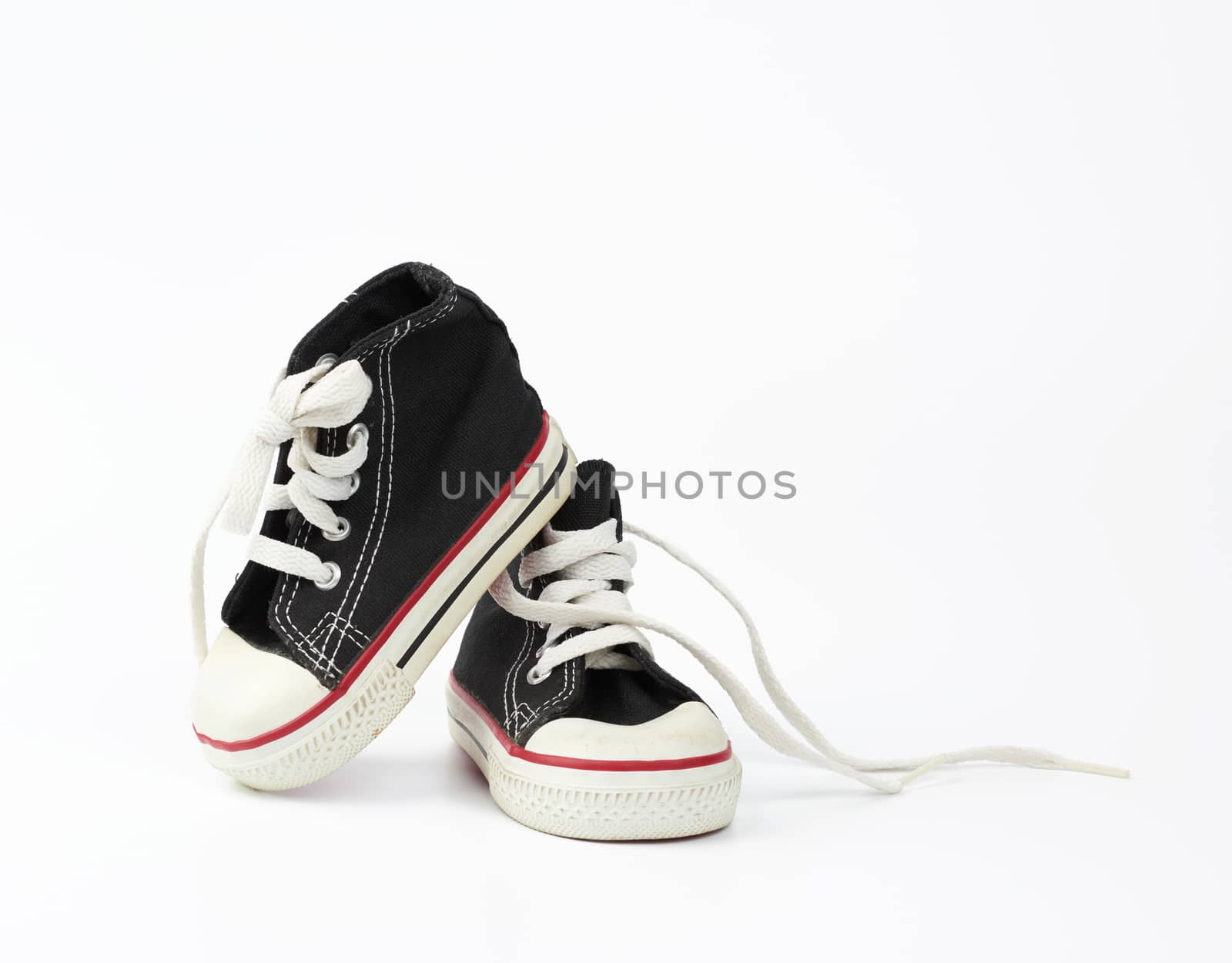 pair of black textile children's sneakers with white untied shoelaces on a white background, shoes are sideways