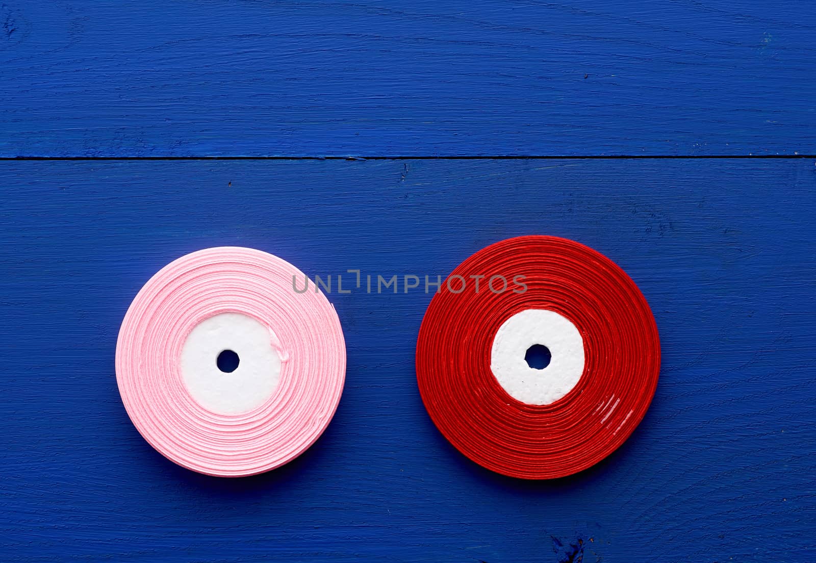 two skeins of pink and red thin silk ribbon on a blue wooden background, decor element, flat lay
