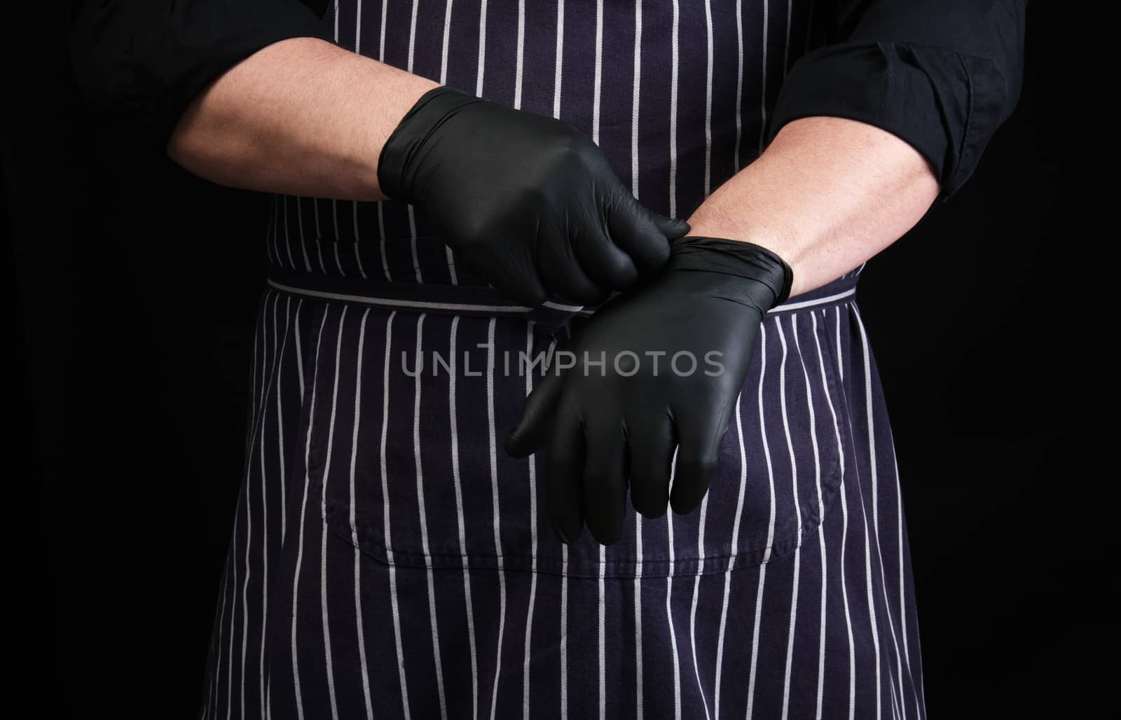 chef man in black uniform and striped apron dresses black latex gloves, low key