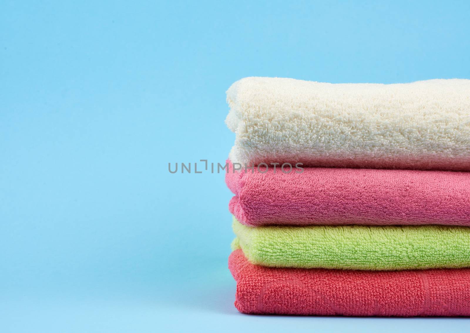stack of colored cotton terry folded towels on a blue background, copy space