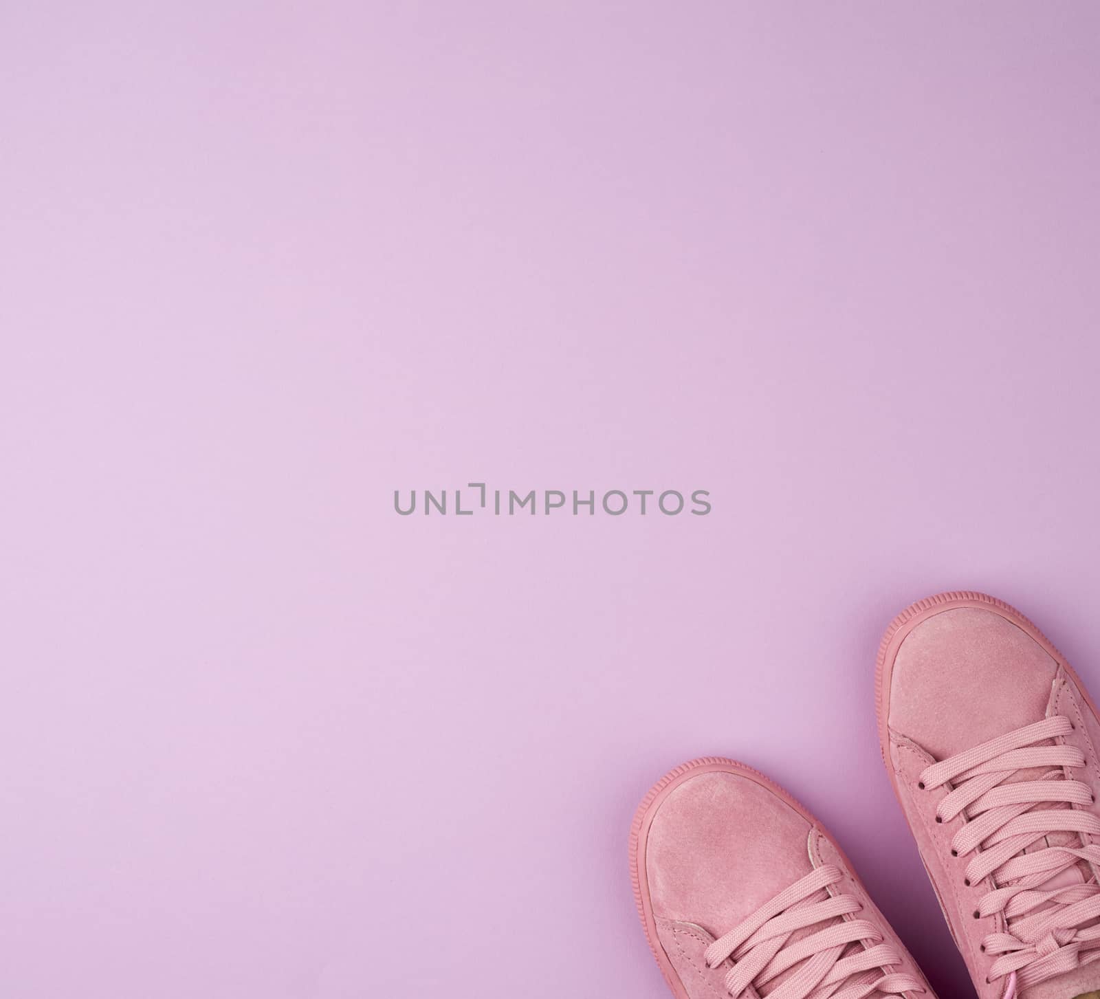 pair of sports pink sneakers with laces on a purple background, top view, place for text 
