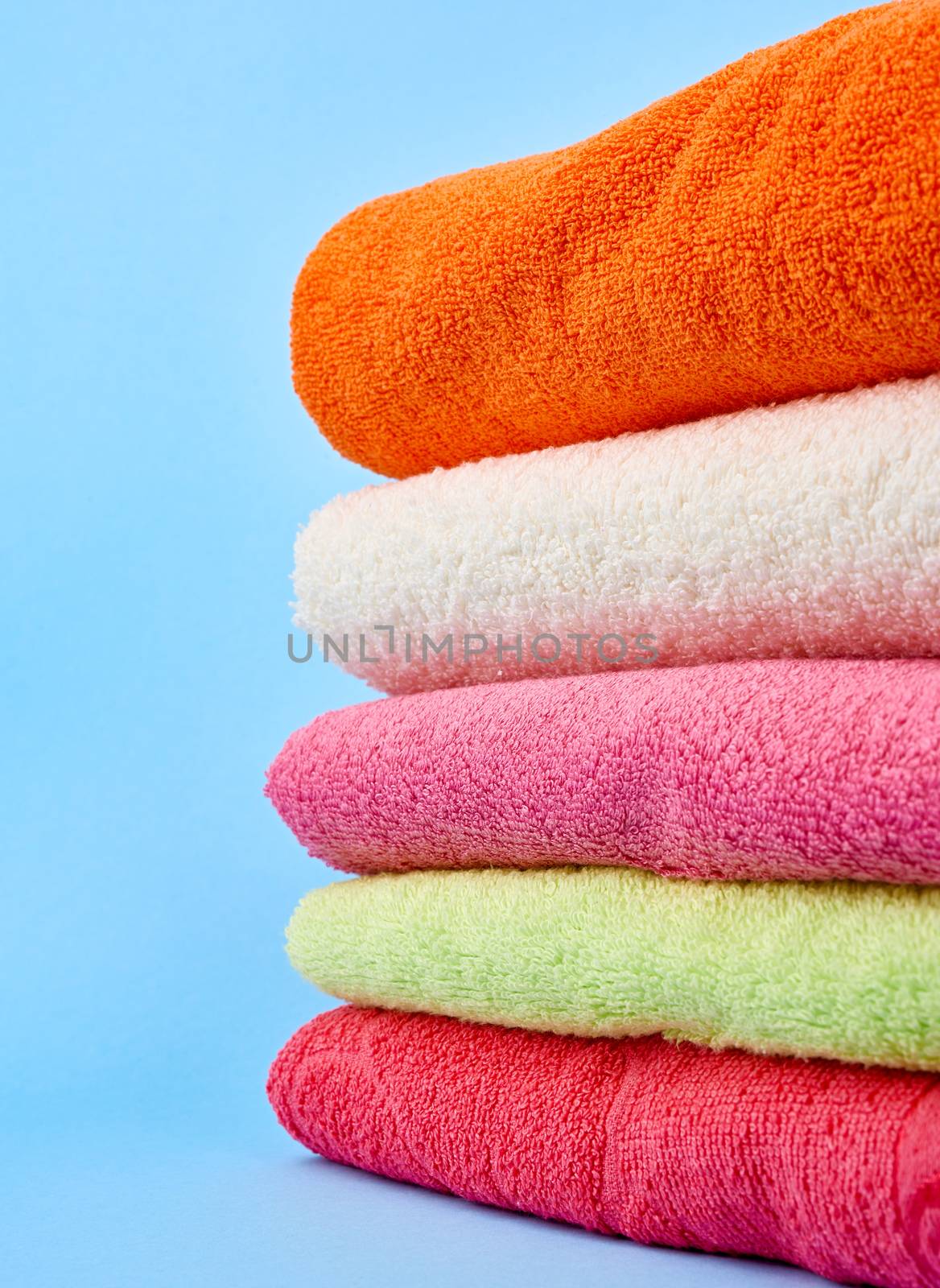 stack of colored cotton terry folded towels on a blue background, close up
