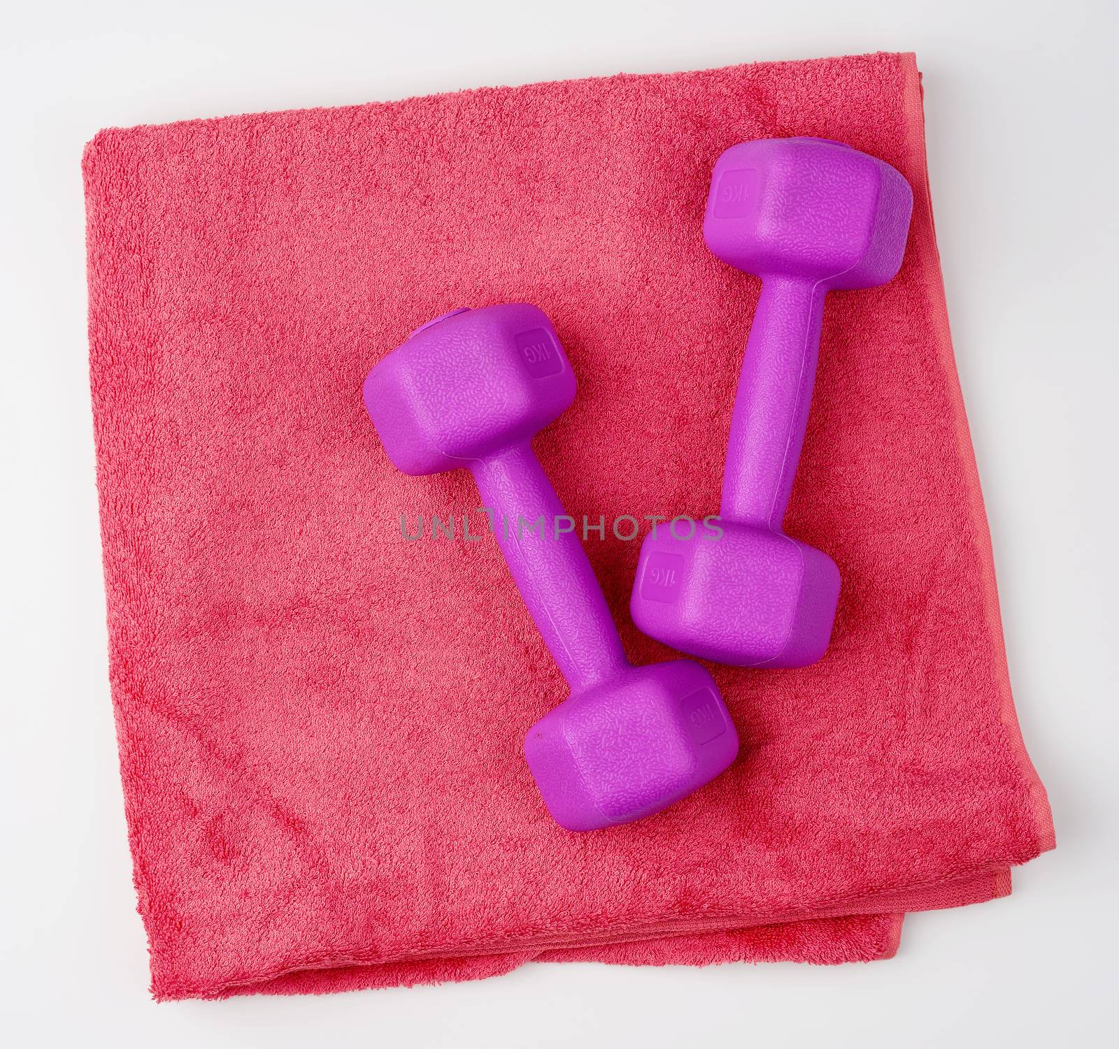 pair of purple plastic dumbbells and pink terry towel on a white background, top view, training equipment