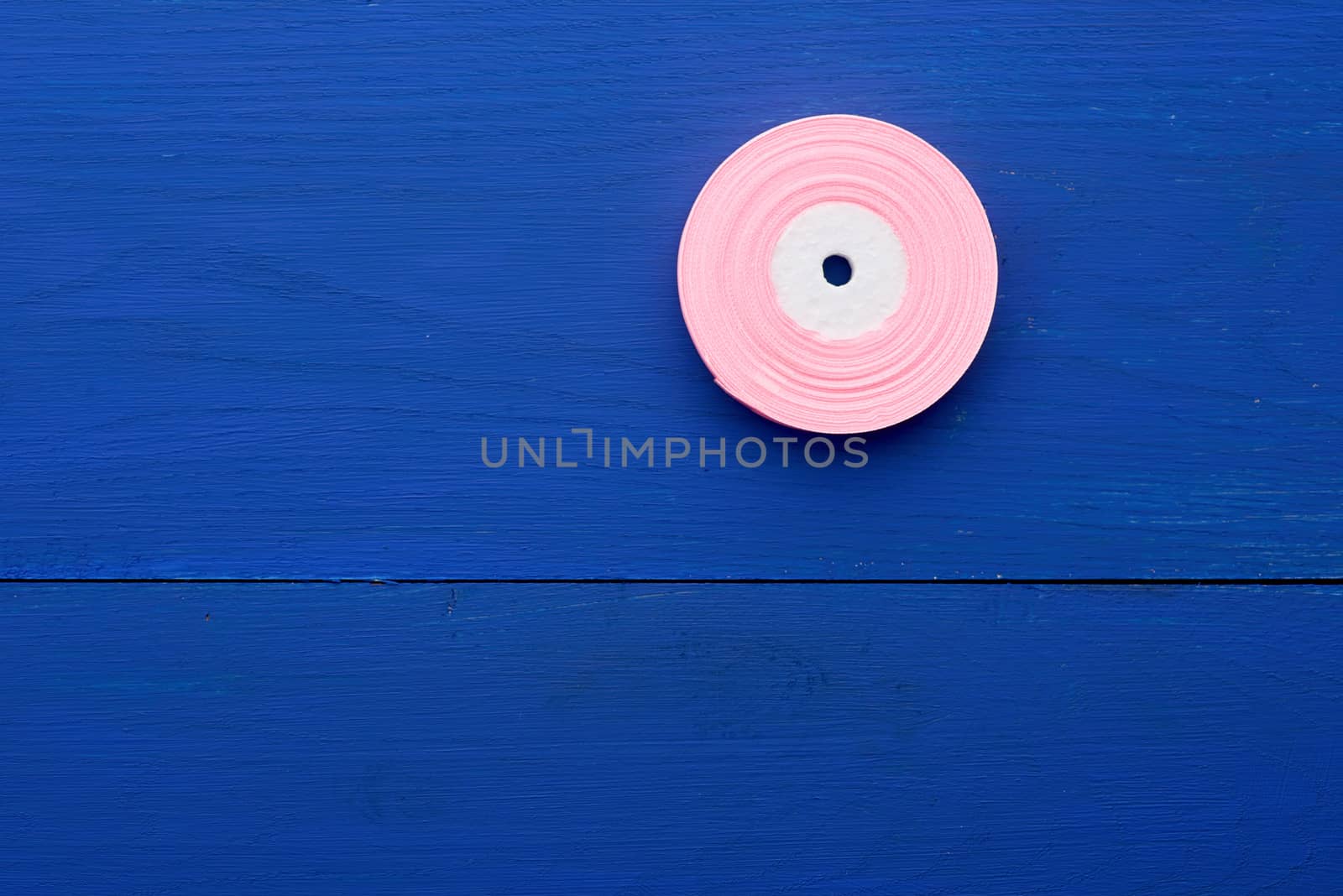 one round bobbin with pink ribbon on a blue wooden background, copy space