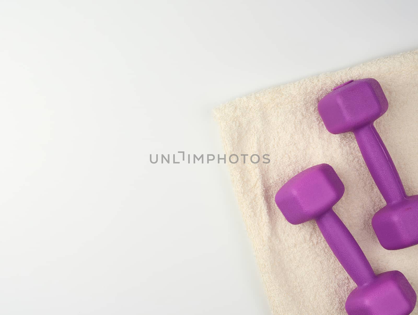 pair of purple plastic dumbbells and white terry towel on a white background, top view, training equipment, copy space