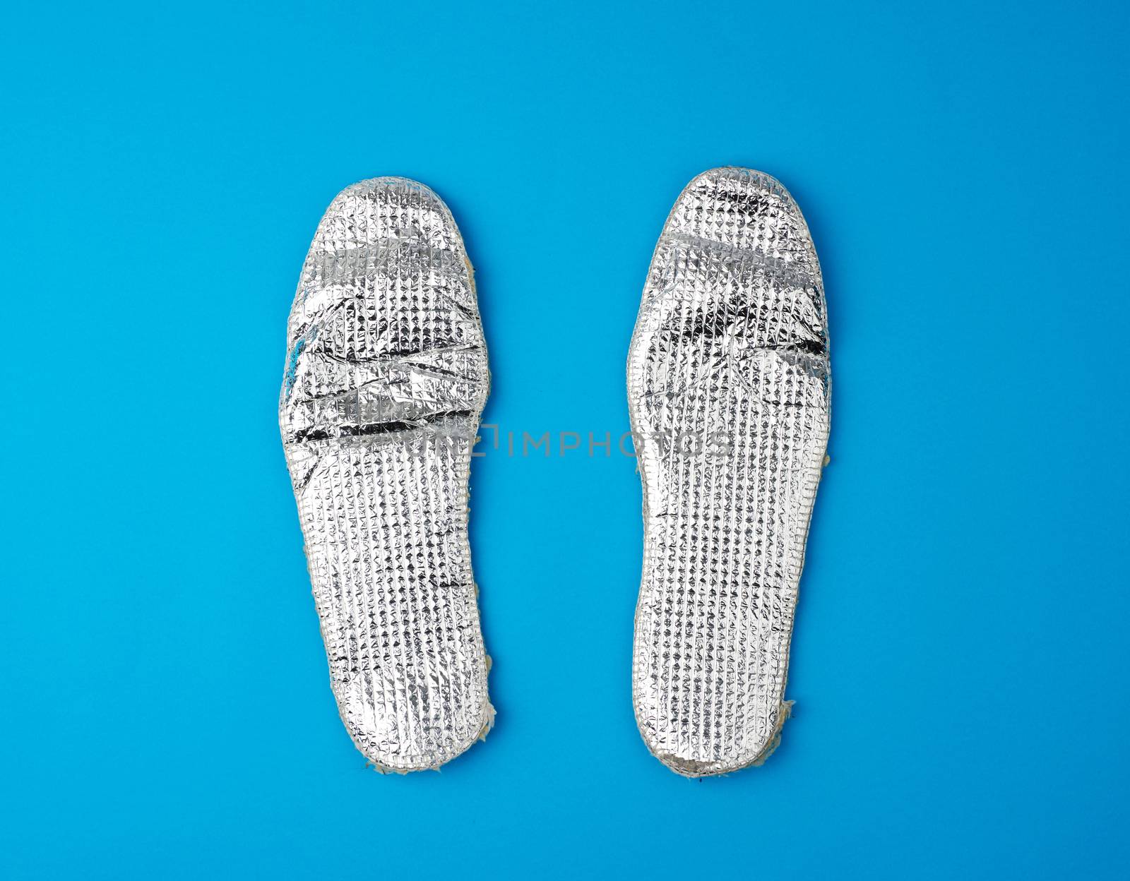 pair of shoe insoles with insulation and foil on a blue background, top view