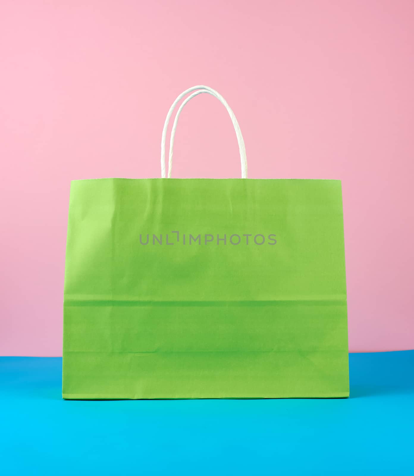 empty green paper bag with white handles for shopping and gifts on blue pink background