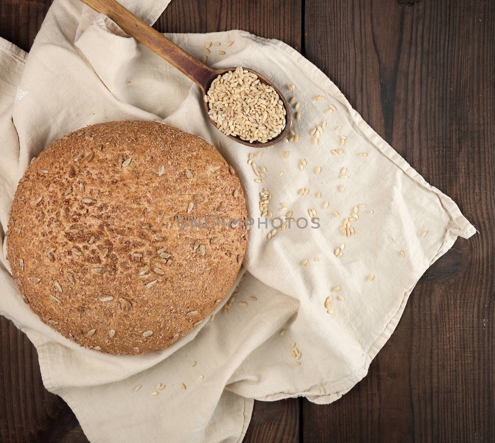 baked round rye bread with sunflower seeds on a beige textile napkin, wooden background, top view