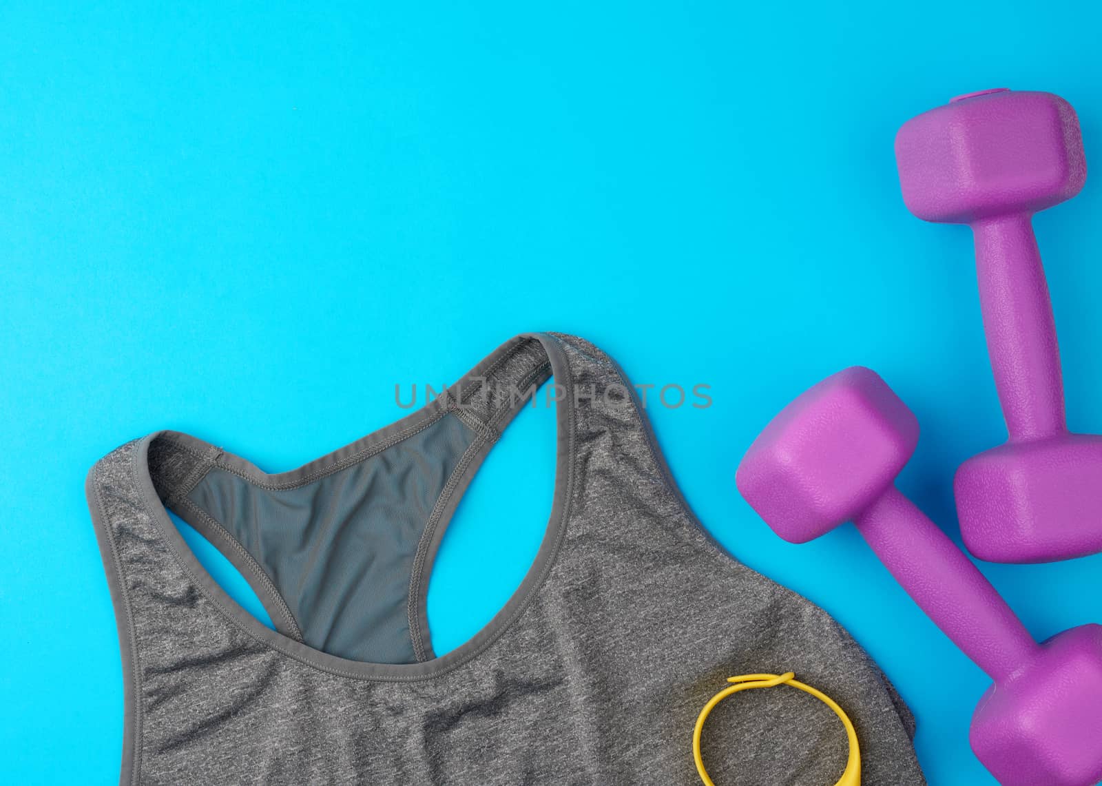 pair of purple plastic dumbbells, gray sports shirt on a blue background, set for sports, flat lay