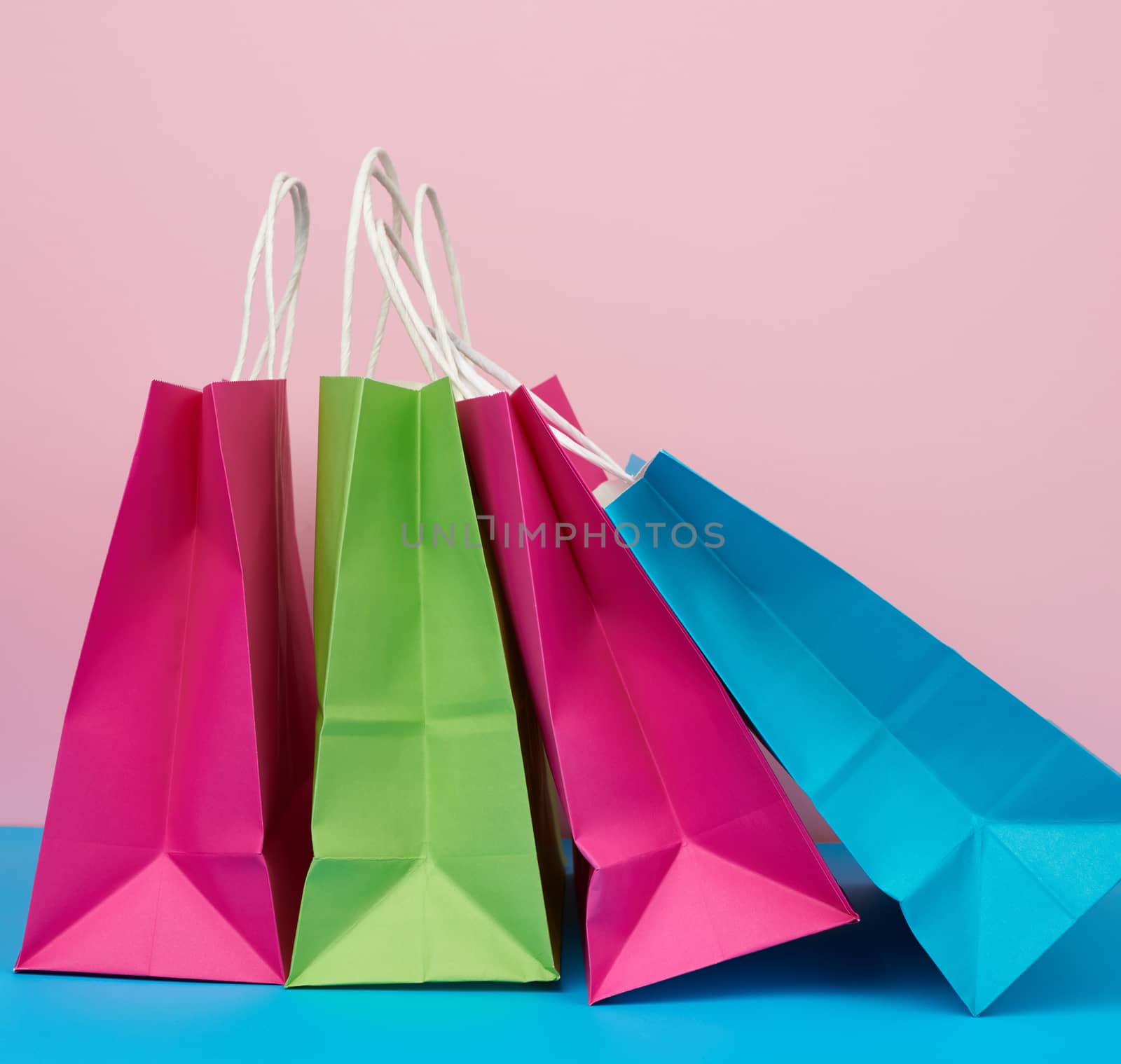 multicolored paper bags for shopping and gifts with white handles stand on a pink-blue background