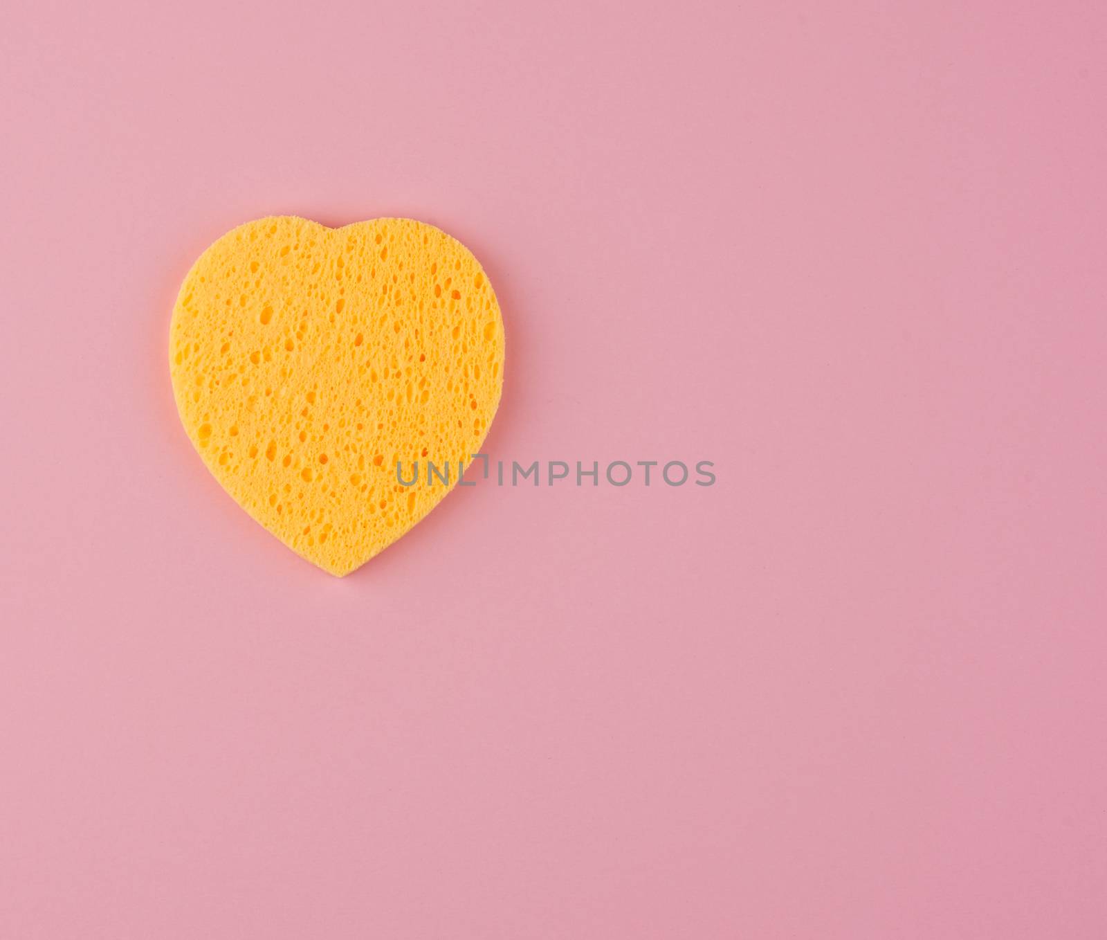 yellow heart shaped sponge for face wash on pink background, copy space
