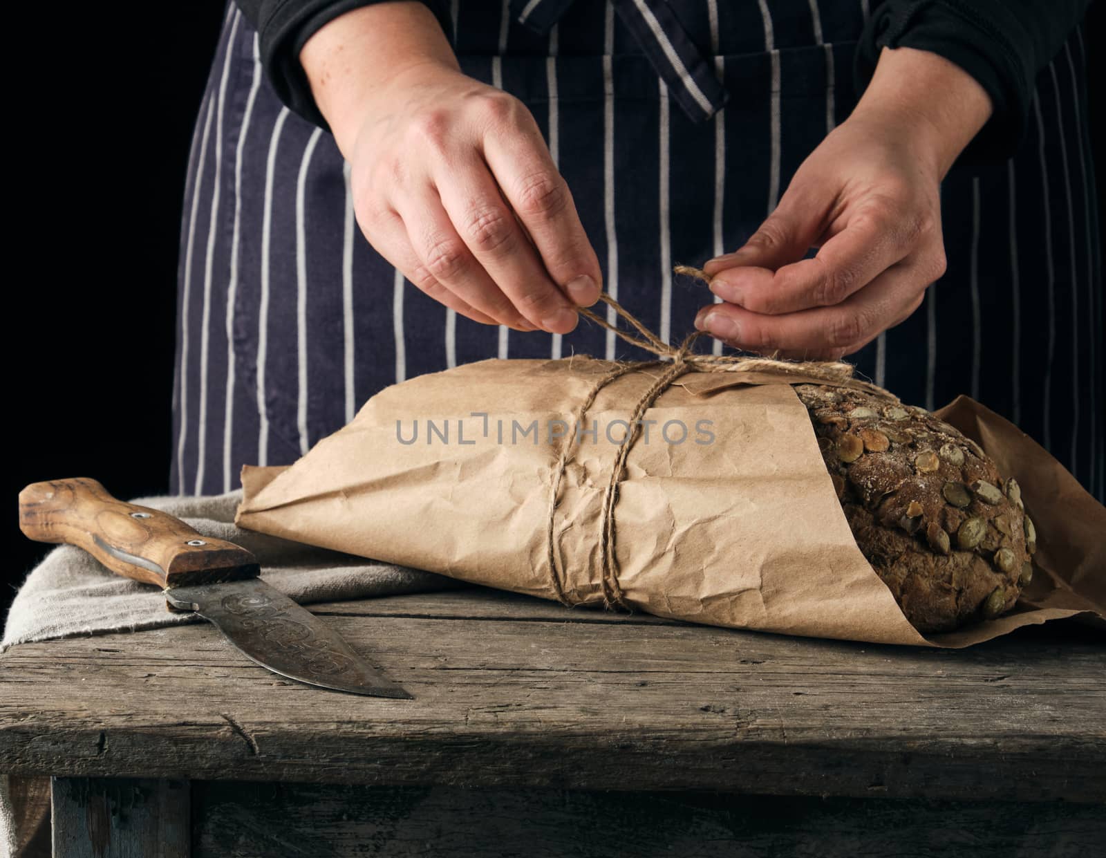 girl in black clothes wraps a whole baked loaf of bread in brown kraft paper and ties 