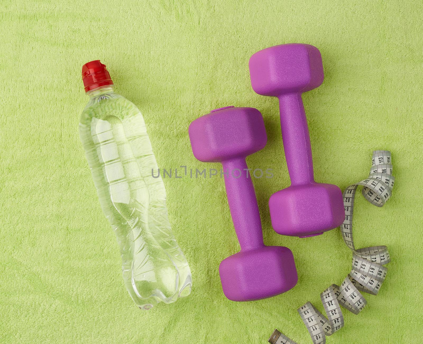 purple dumbbells and a clear plastic bottle of water on a green terry towel, top view, flat lay