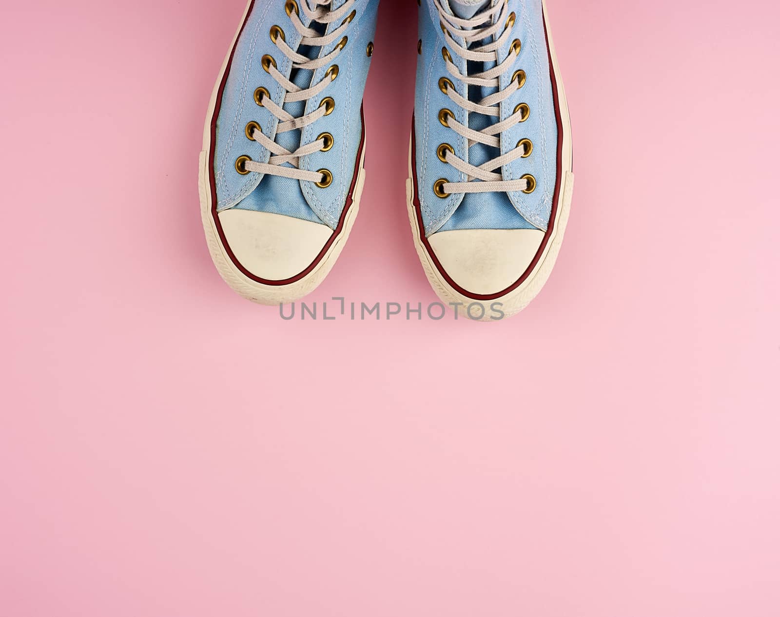 pair of old worn blue sneakers with white laces on a pink background, top view