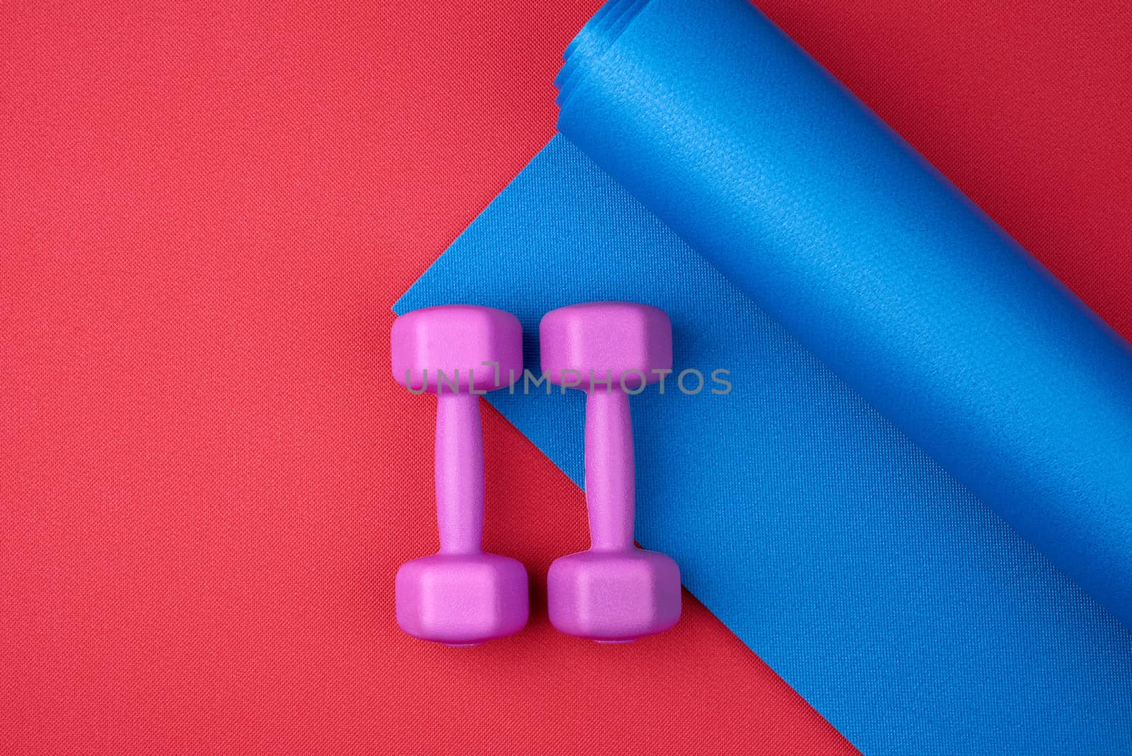 pair of purple plastic dumbbells on a blue neoprene mat, top view, training equipment