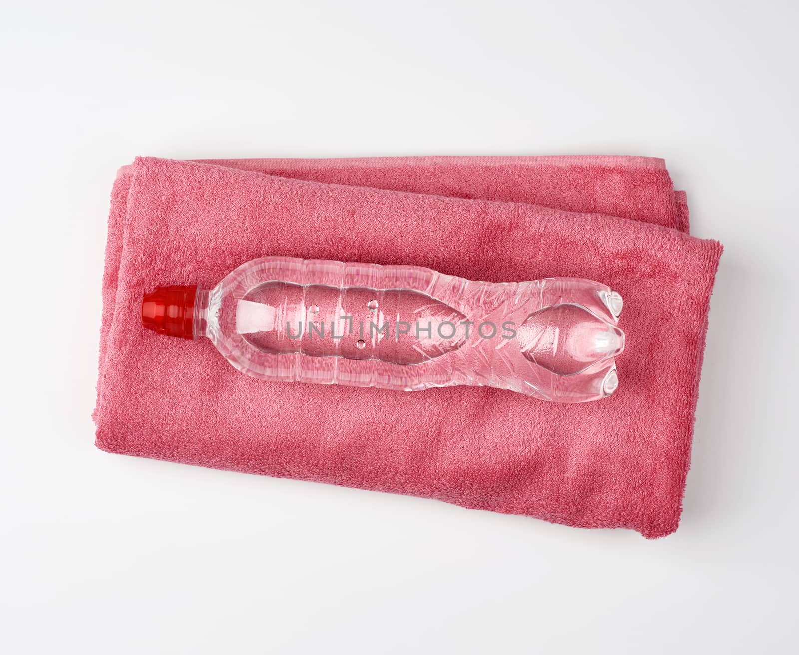 folded pink terry towel and a transparent bottle of water on a white background, concept of drinking more water while doing sports