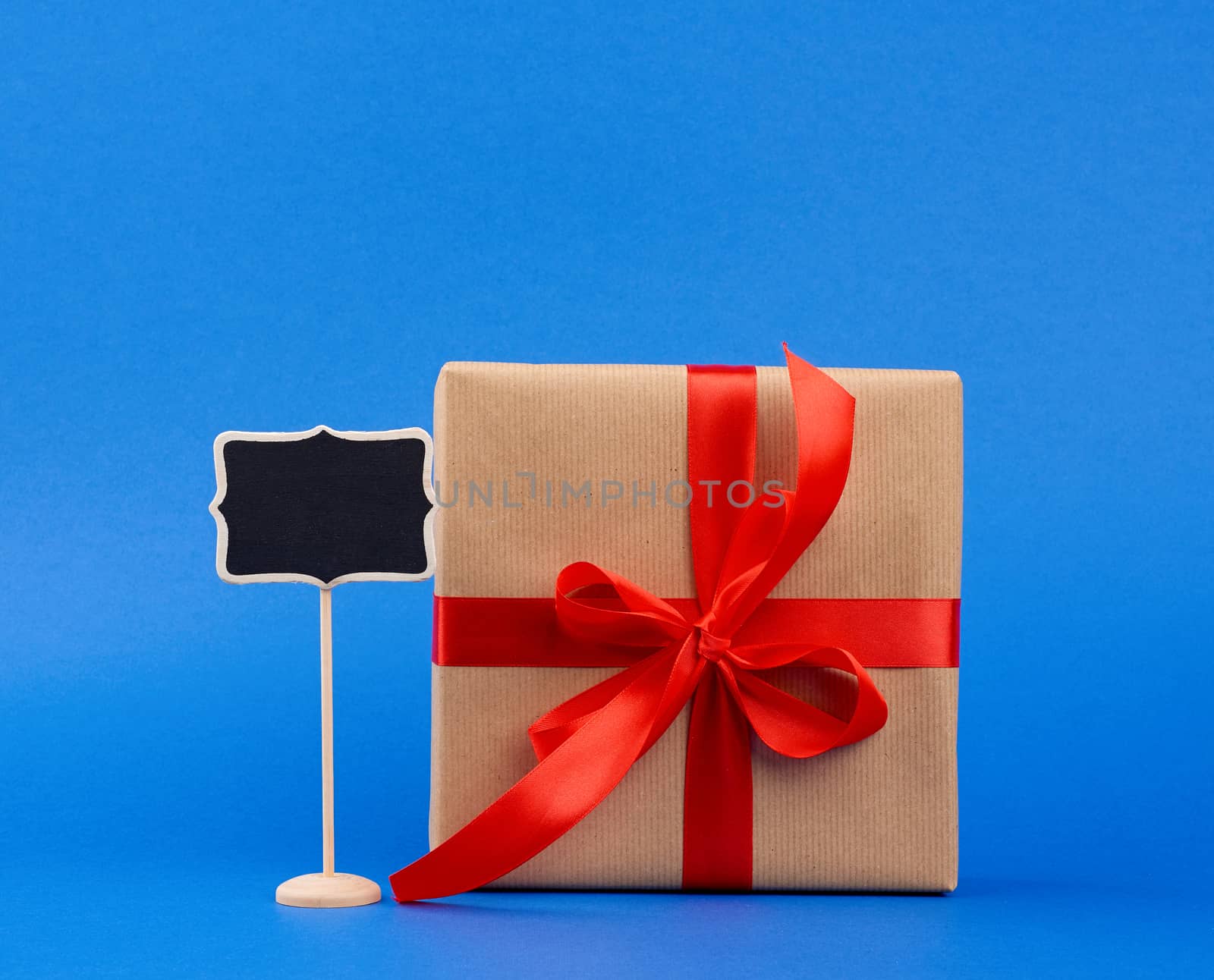 wooden pointer on a stick and a square box wrapped in brown kraft paper and tied with a red silk ribbon, blue background