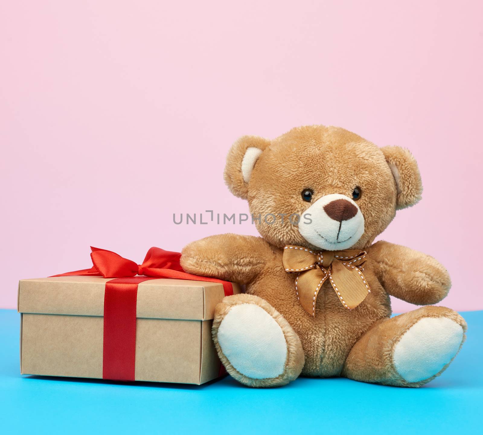 cute little brown teddy bear holds a brown box with a red ribbon on a blue background