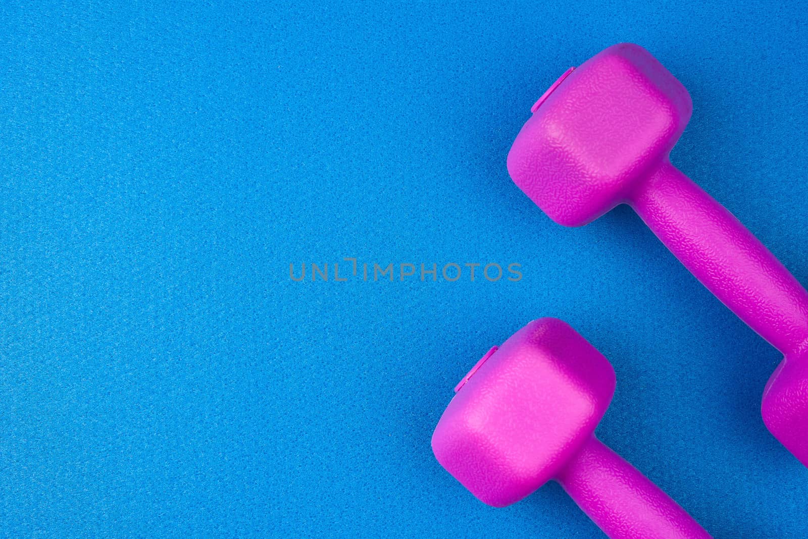 pair of purple plastic dumbbells on a blue neoprene mat, top view, training equipment, copy space
