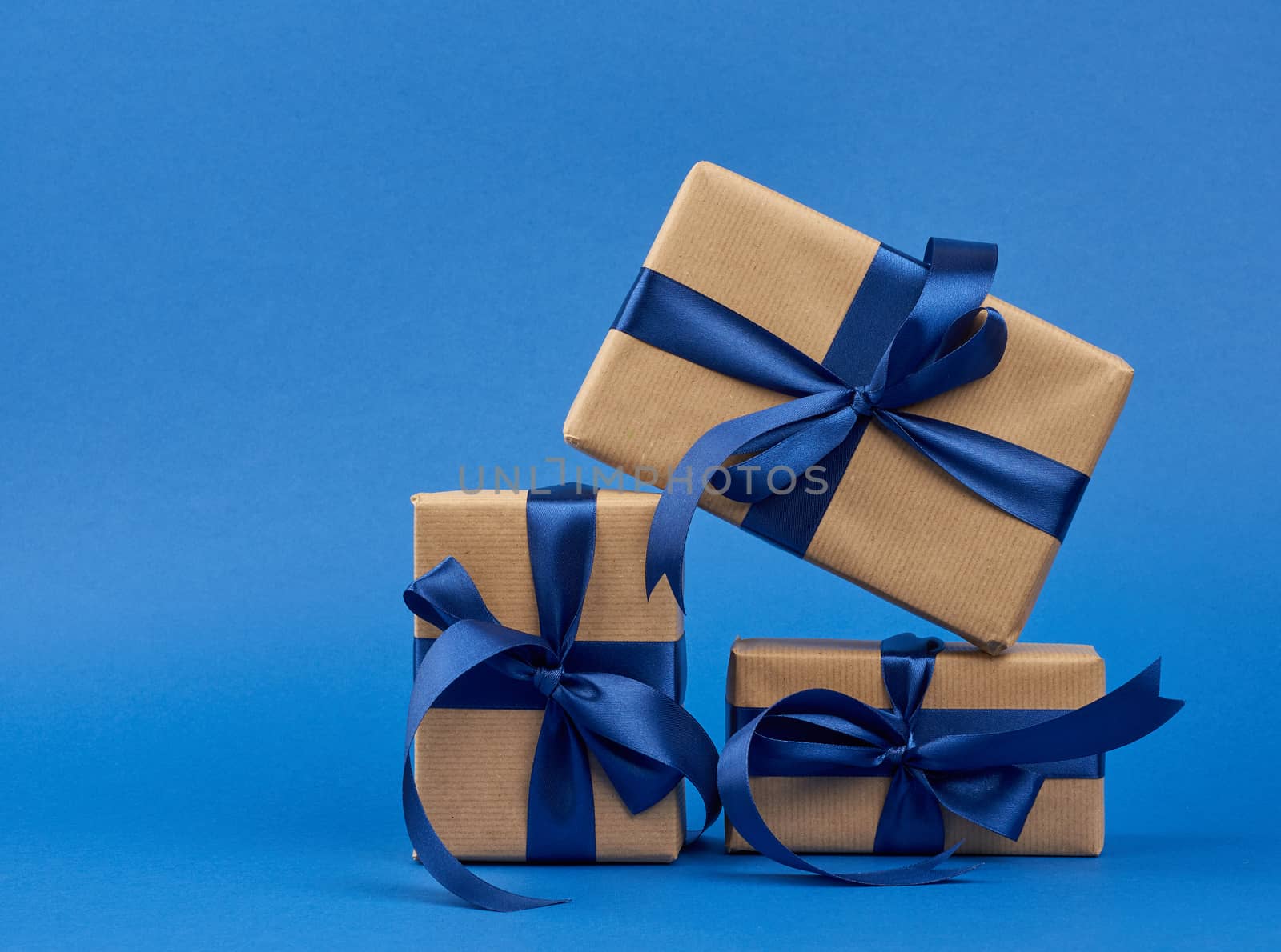 rectangle box wrapped in brown kraft paper and tied with a silk blue ribbon, gift on a dark blue background, copy space