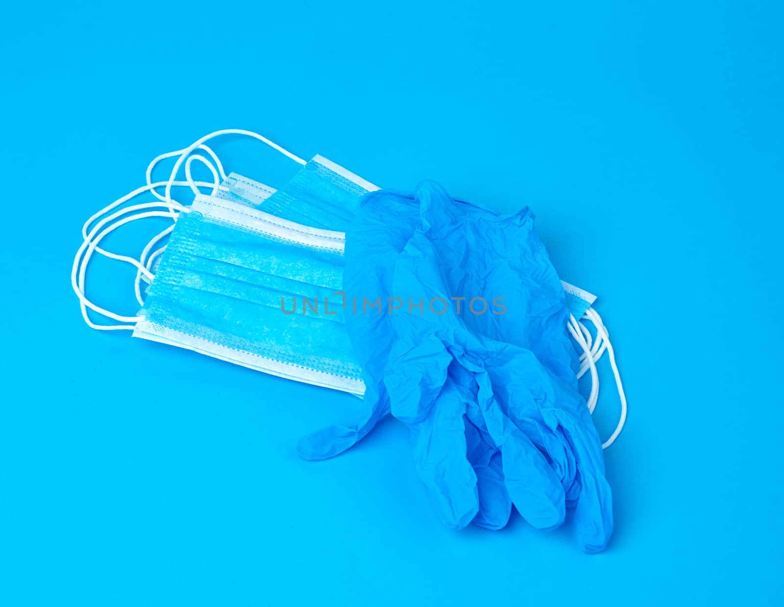 disposable gloves and stack of medical masks made of non-woven material with white rubber bands on a blue background, protective accessory for the respiratory tract from the virus