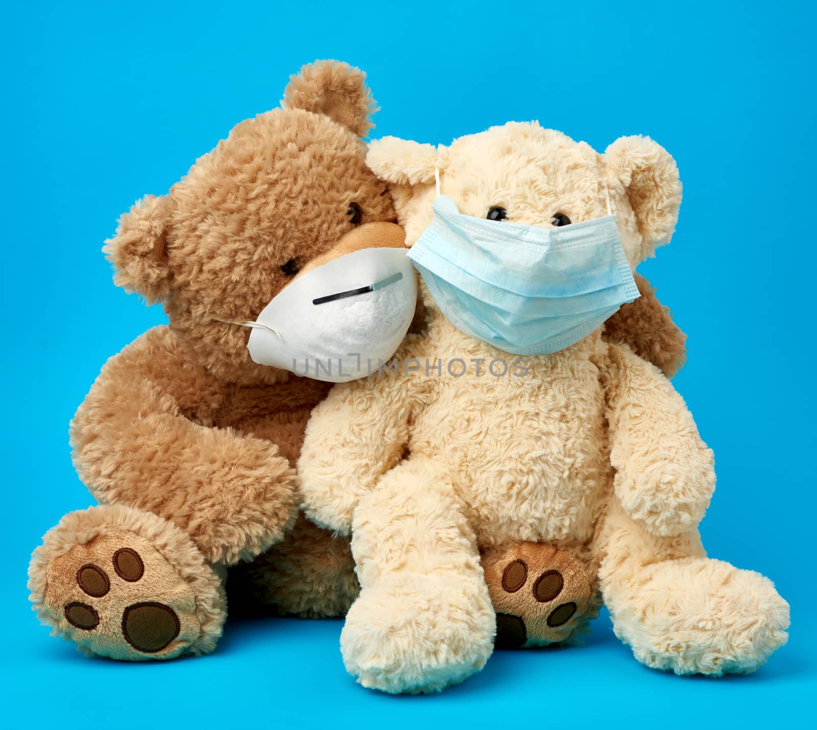 big teddy bears are sitting in medical masks on a blue background, concept of protection from respiratory disease, virus and individual respiratory protection