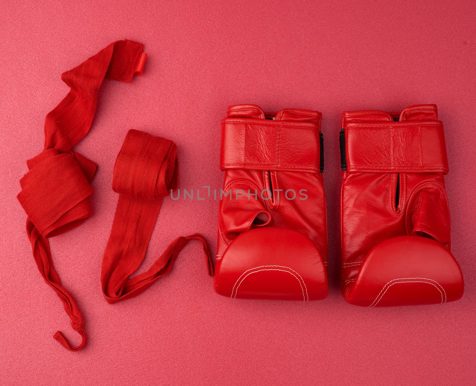 pair of red leather boxing gloves and a textile red elastic bandage for hands lie on a neoprene mat, sports set