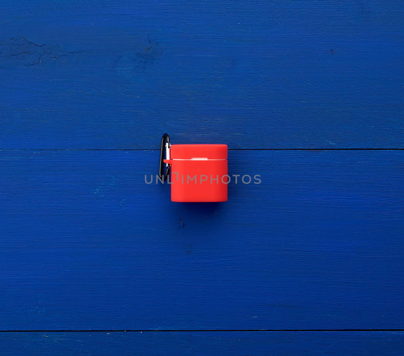 white wireless headphones, charging box and red silicone case on a blue wooden background, top view