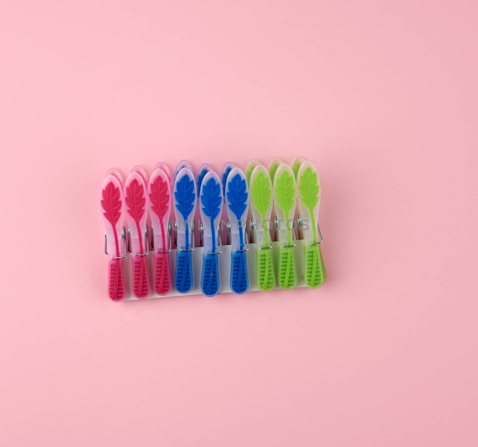 plastic multi-colored clothespins on a pink background, top view
