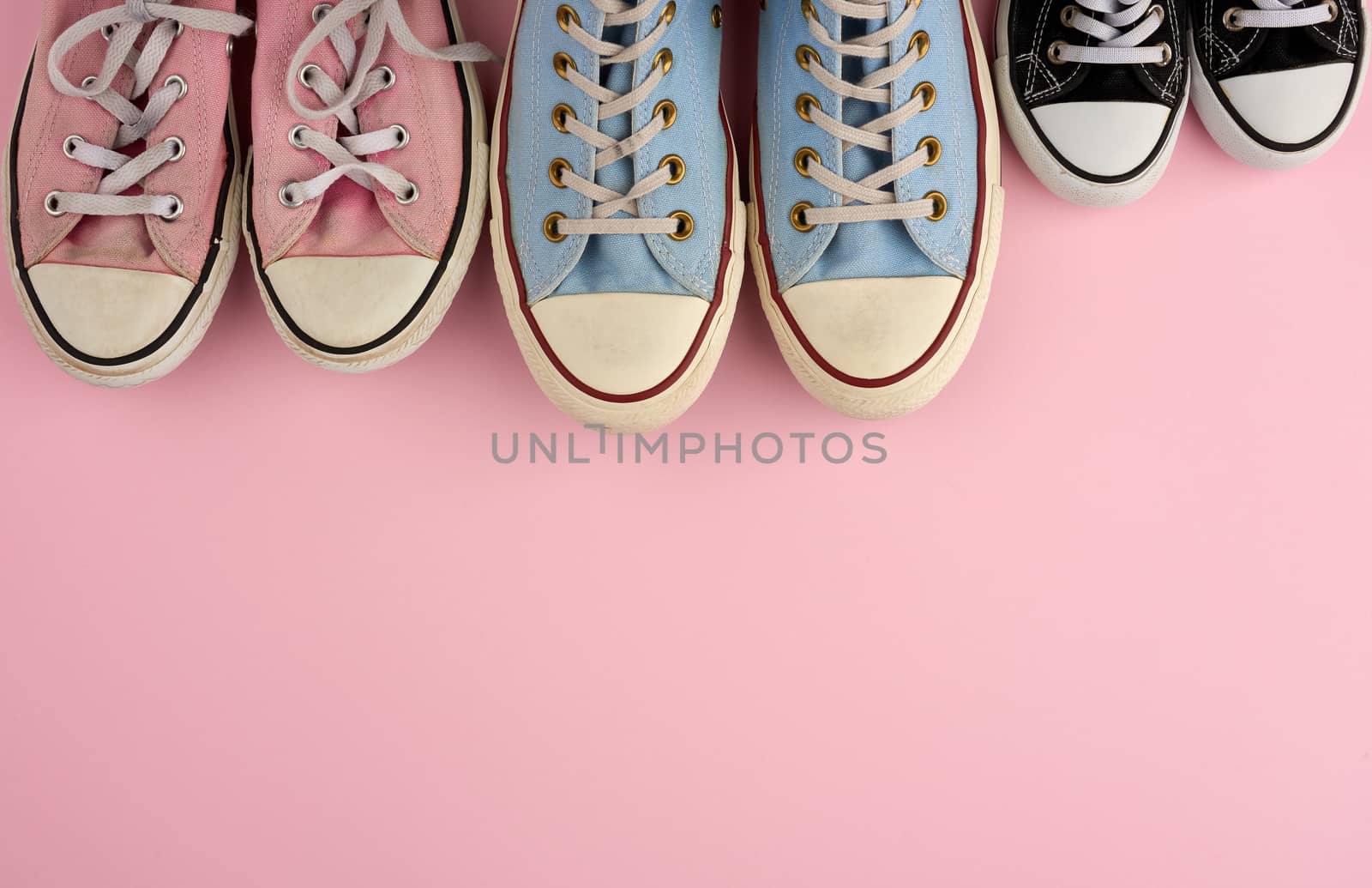 many multi-colored well-worn textile sneakers of different sizes on a pink background, top view, concept, family and team, friendship, copy space