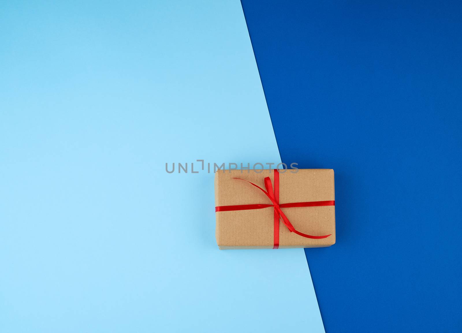box wrapped in brown kraft paper and tied with a red thin silk ribbon on a blue background, holiday Valentine's Day.  Anniversary, birthday.