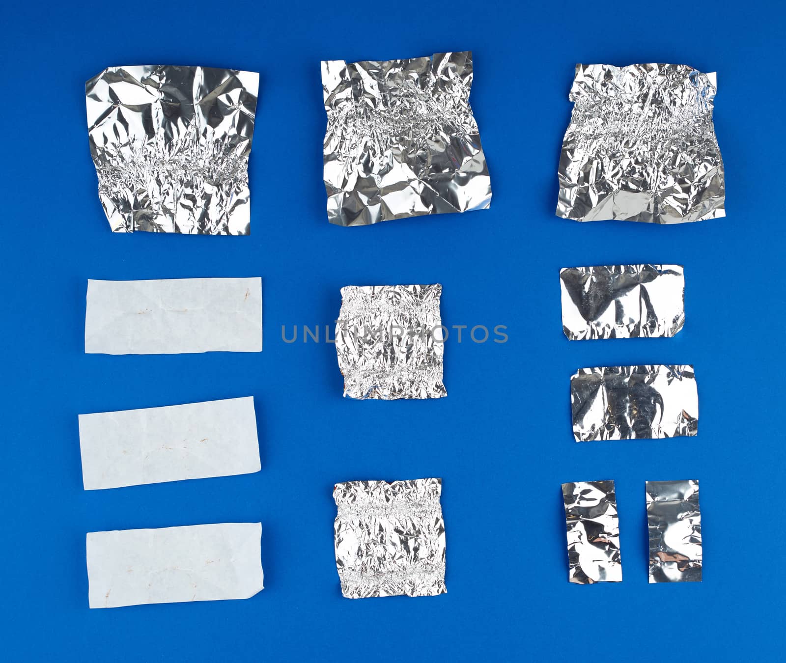 various crumpled white paper and foil used candy wrappers on a blue background, top view