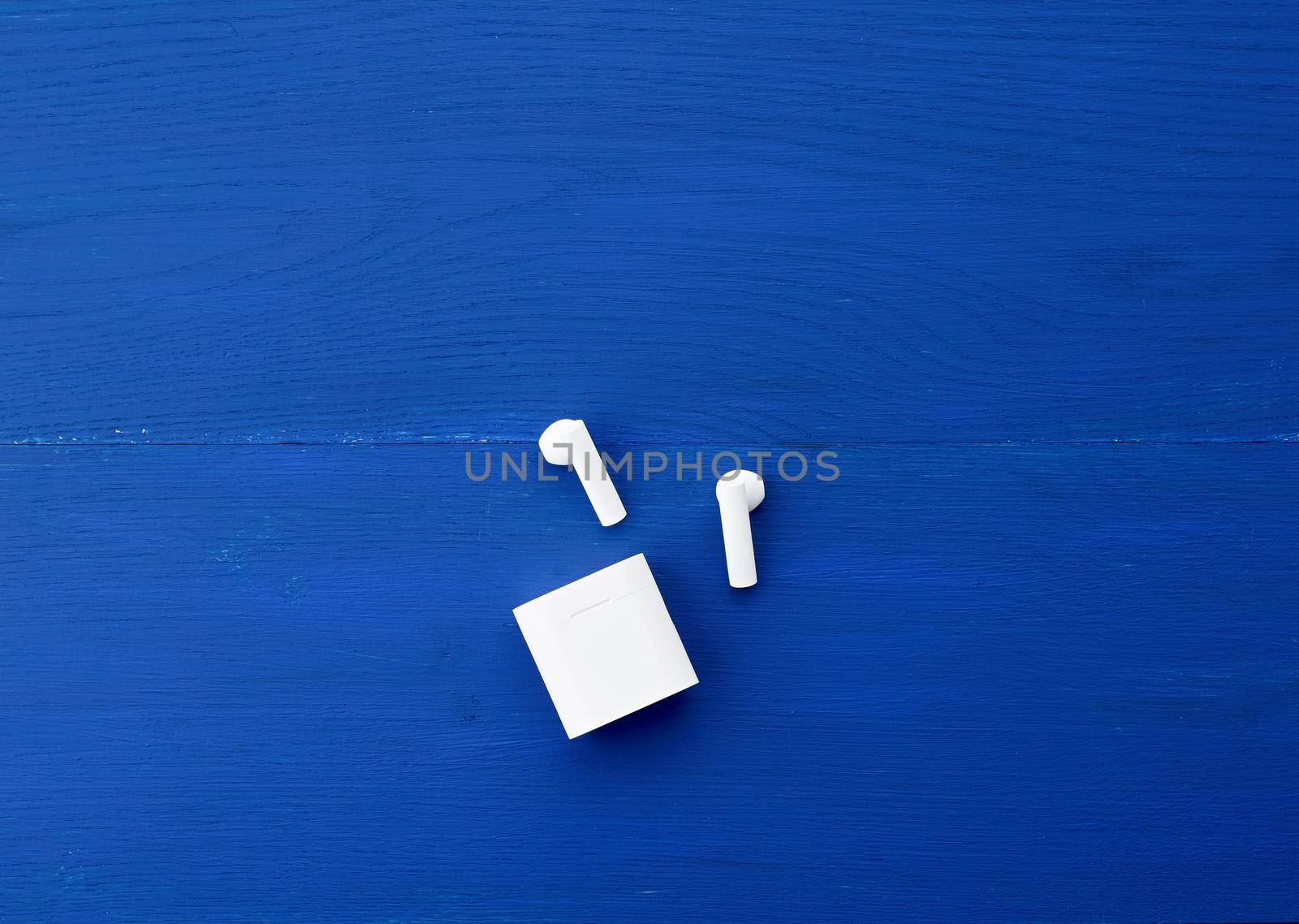white wireless headphones and charging box on a blue wooden background, top view