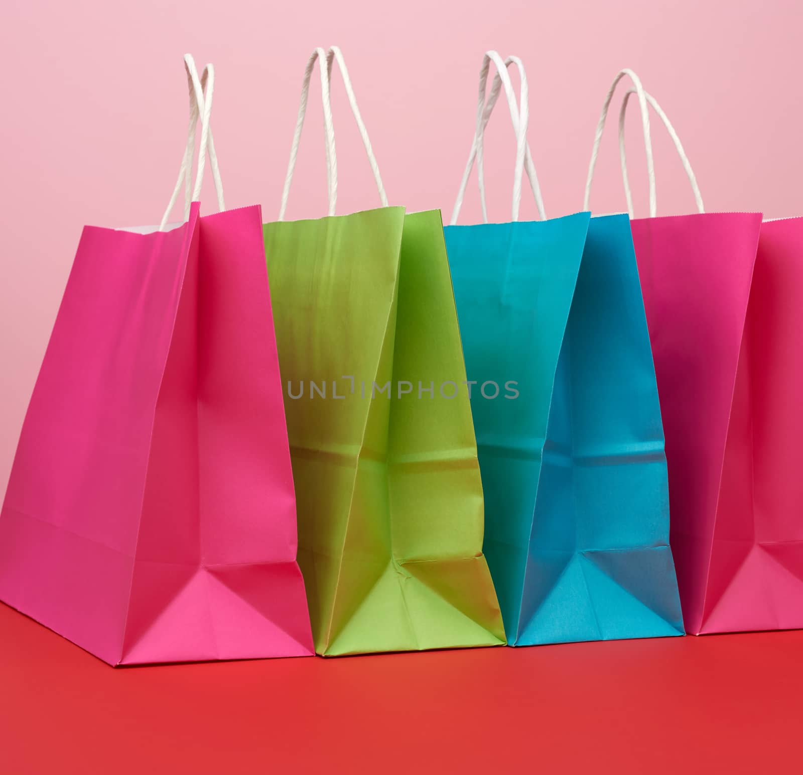 empty multicolored paper bags for shopping and gifts with white handles stand on a red-blue background, copy space