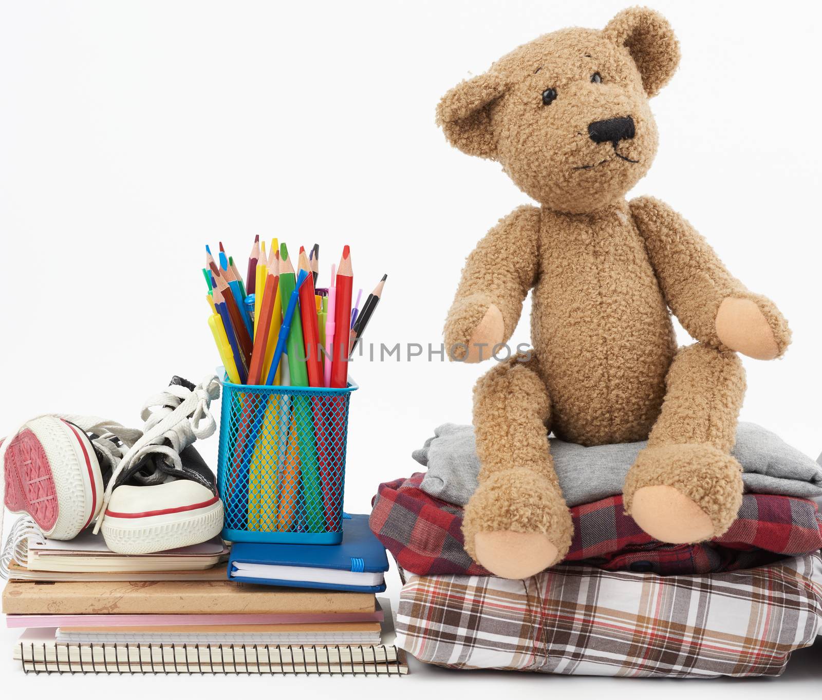 stack of folded clothes, sports sneakers, stationery and a brown teddy bear on a white background, concept for helping the needy, donation