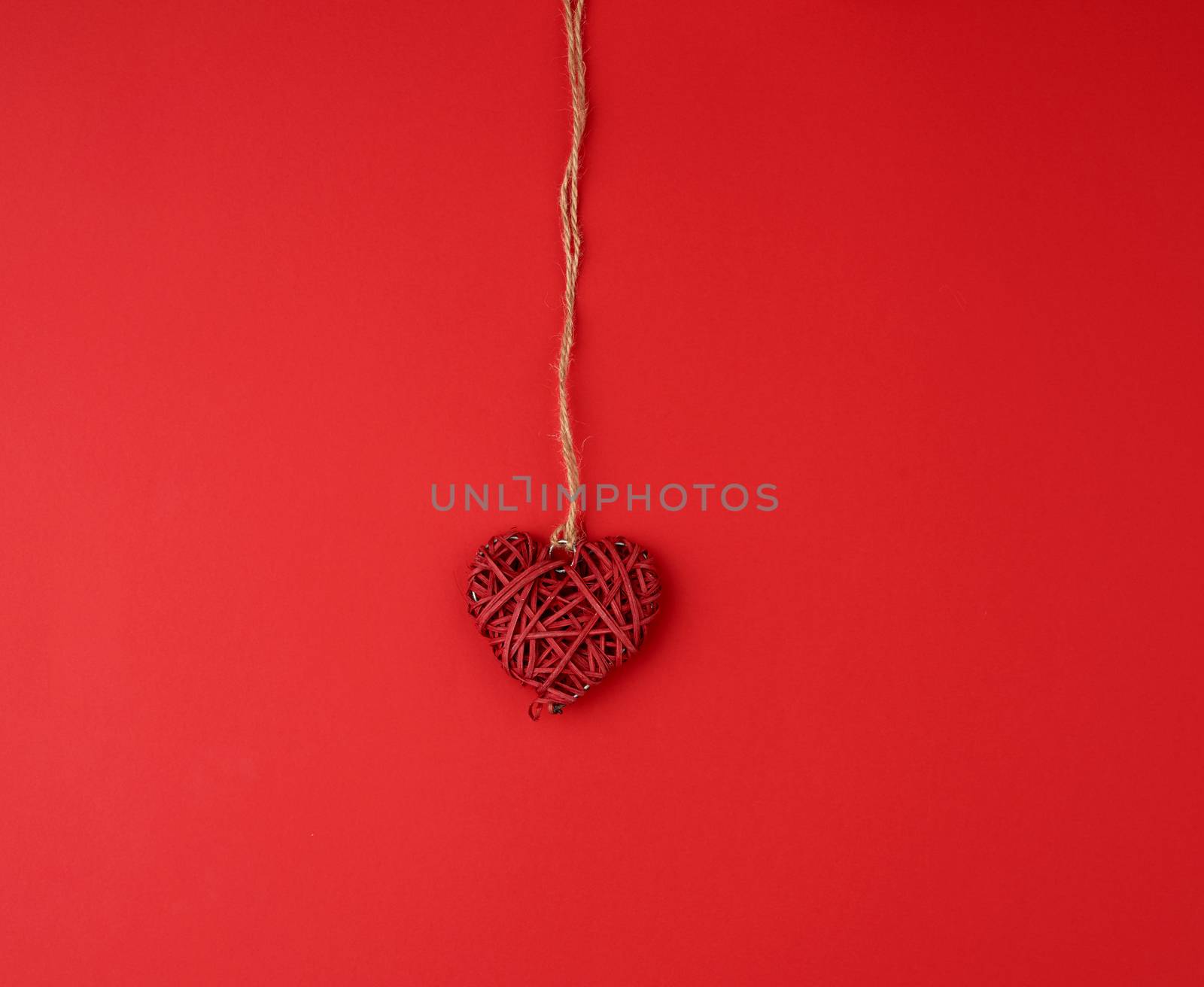red wicker decorative heart hanging on brown rope, red festive background for Valentine's day