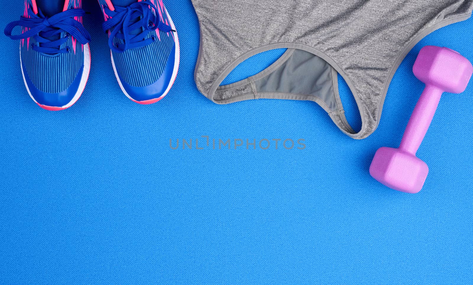 purple plastic dumbbells, gray sports shirt, blue sneakers on a blue background, set for sports, flat lay