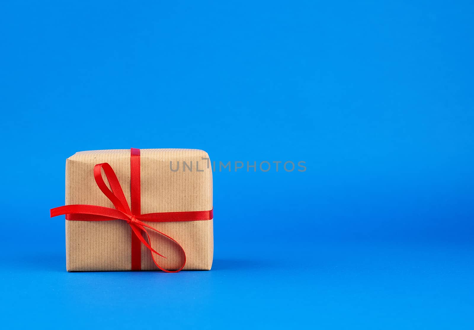 box wrapped in brown paper and tied with a red bow, gift on a blue background. Great design for any purposes. Holiday background. Valentine gift.