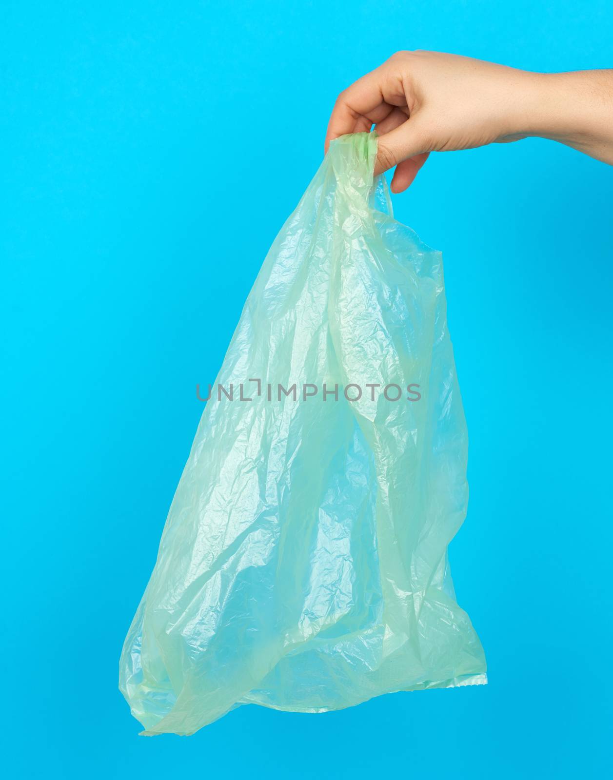 hand holds an empty green plastic bag on a blue background by ndanko