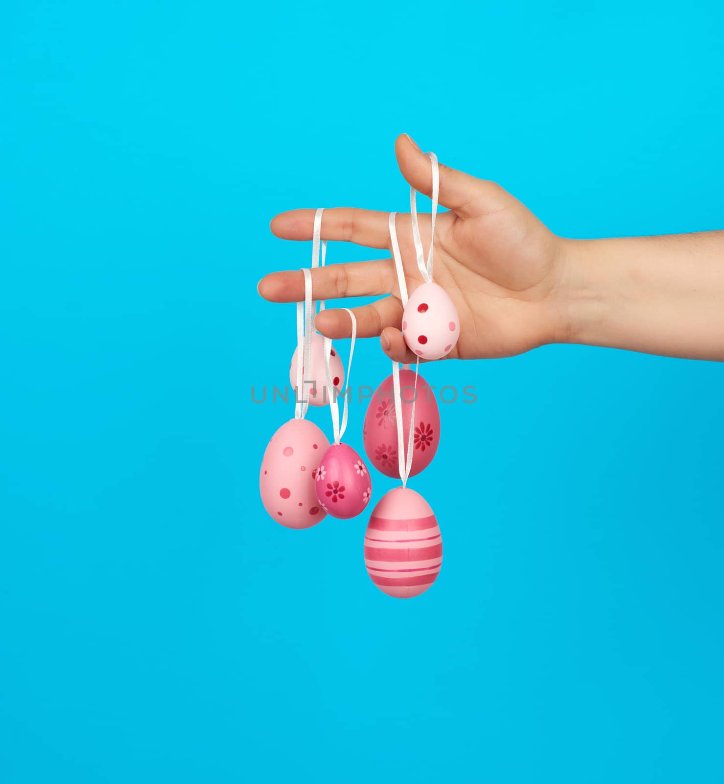 female hand holds easter colored pink eggs on a rope by ndanko