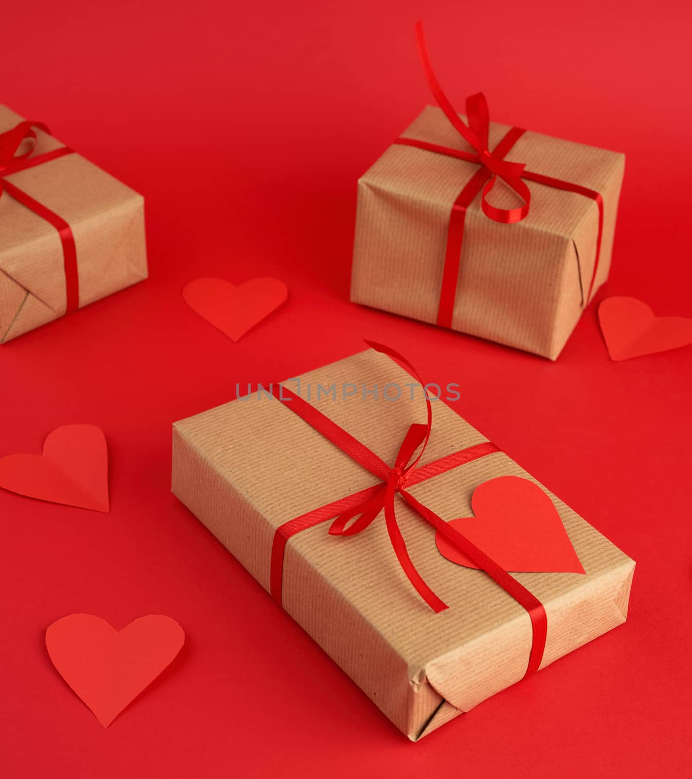 box wrapped in brown kraft paper and tied with a red thin silk ribbon, cut out of paper hearts, red background, gift for Valentine's Day, birthday