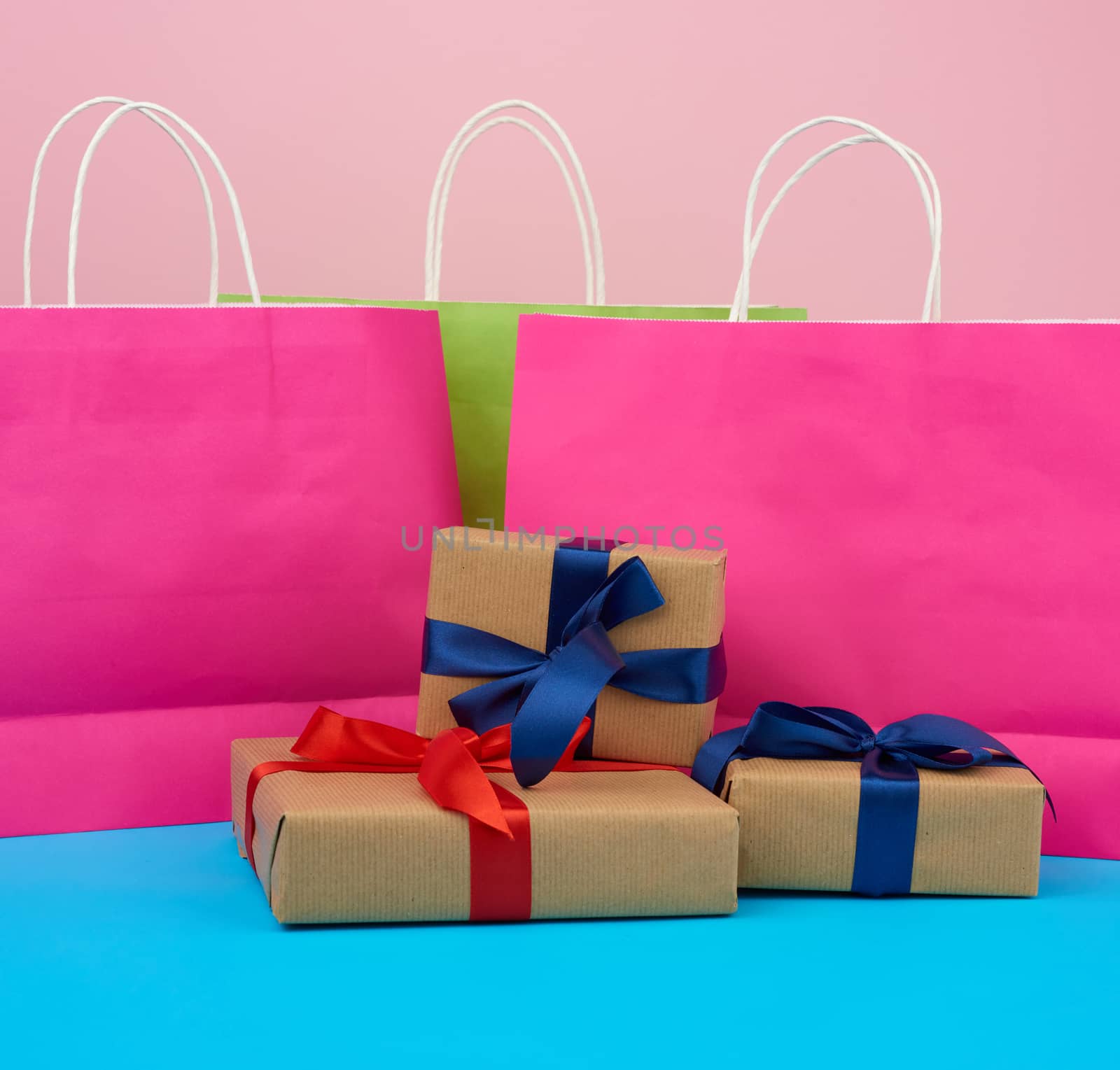 brown paper box with a gift and multi-colored paper bags for shopping and gifts with white handles stand on a pink-blue background
