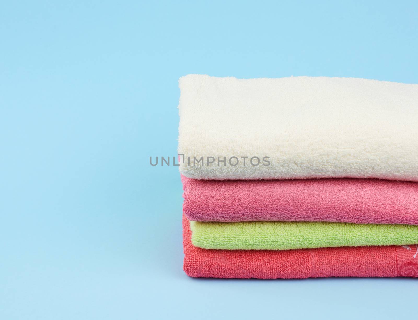 stack of colored cotton terry folded towels on a blue background, copy space