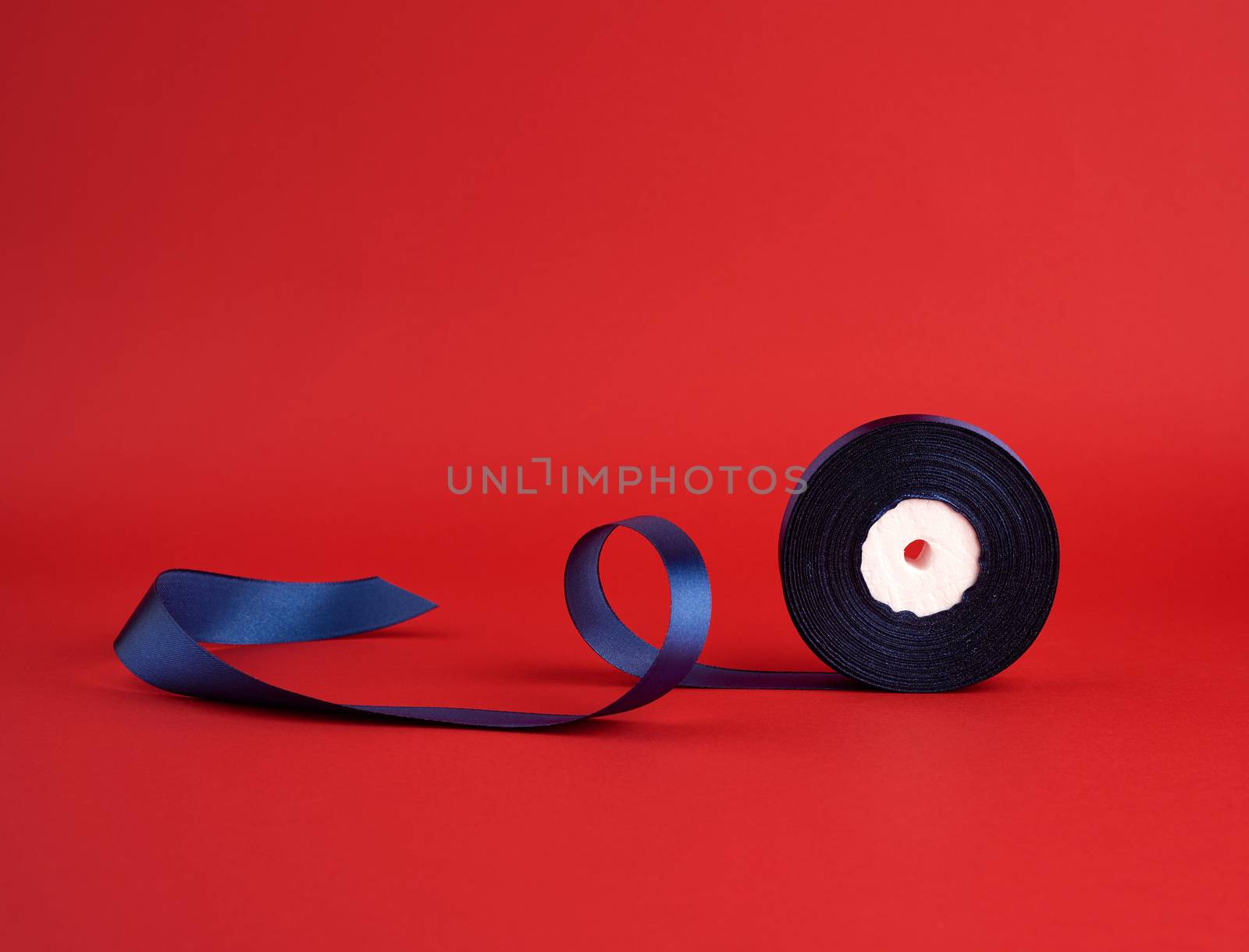 spool of twisted dark blue silk shiny ribbon on a red background, festive design element